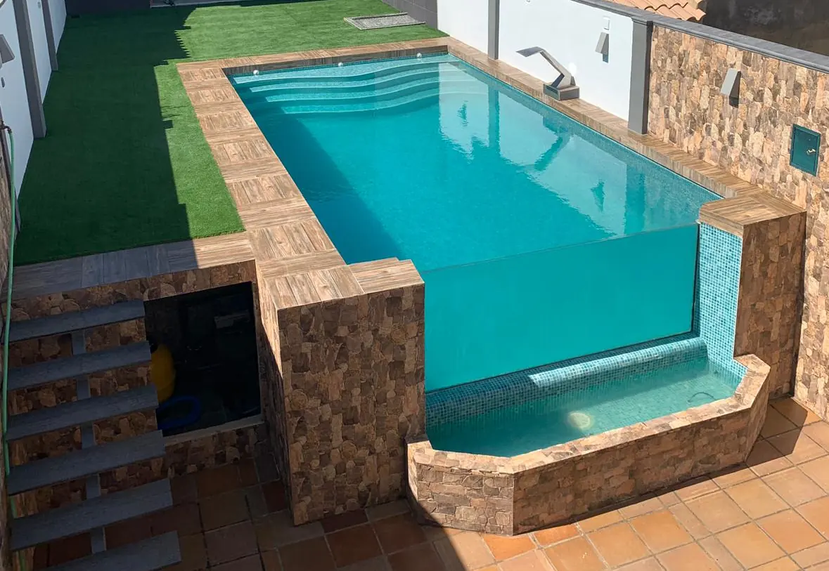 Piscina construida por Piscinas Andalusí con muro de cristal, piedra natural y césped