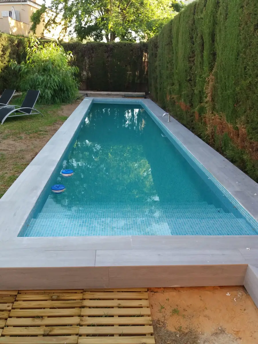 Piscina alargada con playa de obra y coronación clara